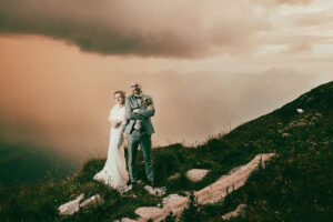 Brautpaar steht auf einem Berggipfel kurz vor einem herannahenden Gewitter, dramatische Hochzeitsaufnahme