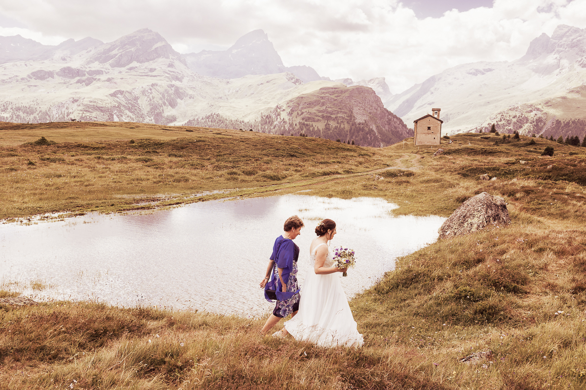 Braut mit Begleitung auf dem Weg zur Kapelle Son Roc auf der Alp Flix, festgehalten während einer Hochzeit von Hochzeitsfotograf Adrian Flütsch.