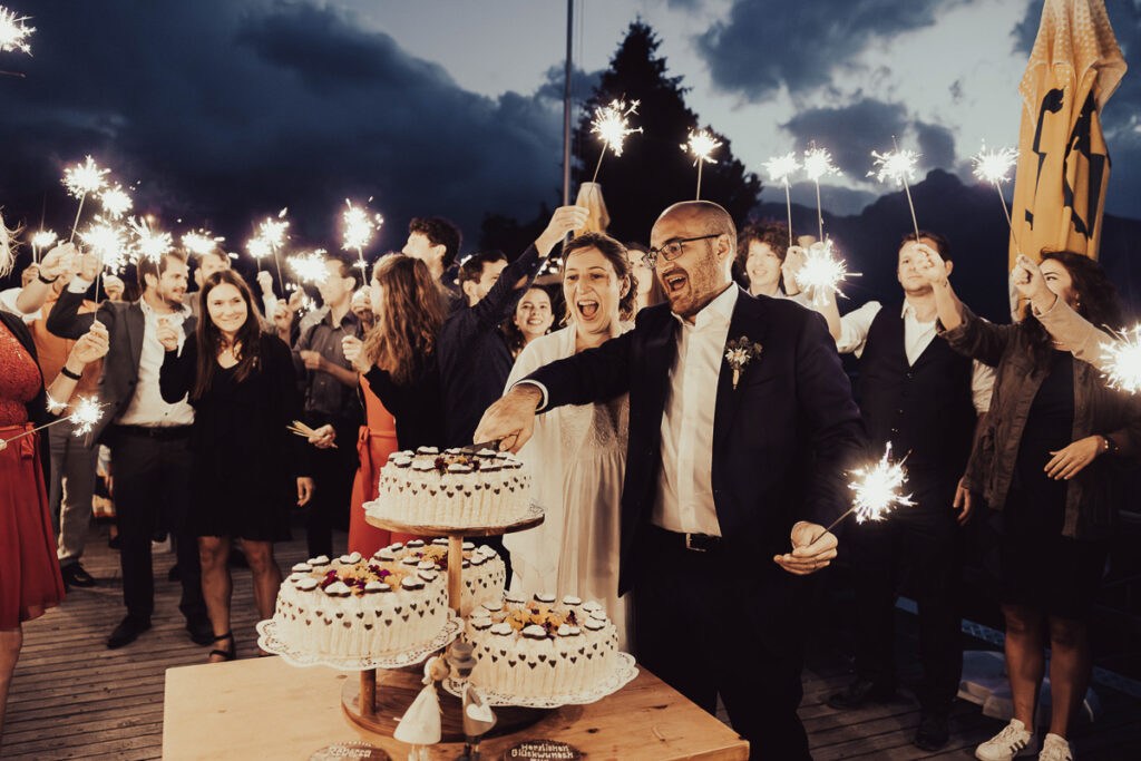 Umgeben von Gästen mit Wunderkerzen schneidet das glückliche Brautpaar Ihre Hochzeitstorte an.