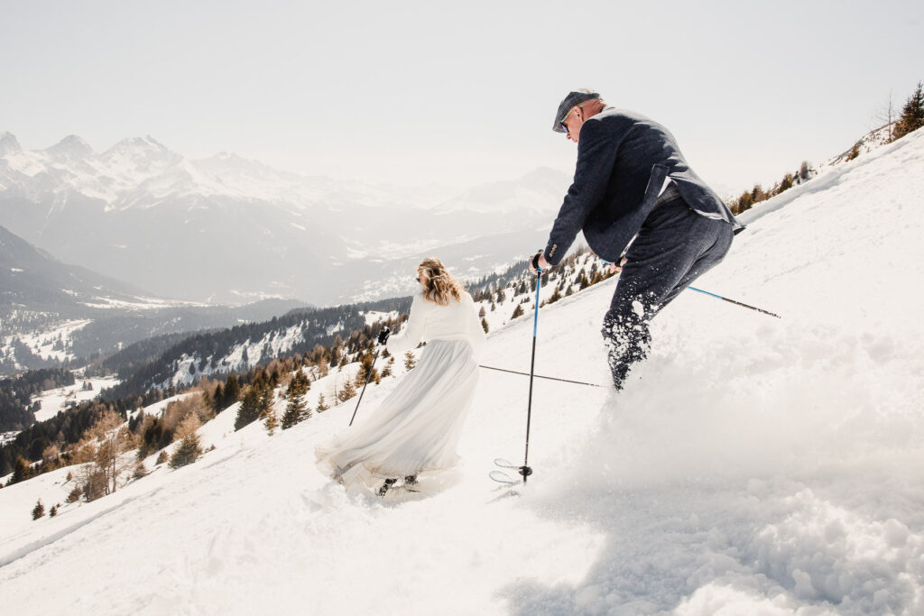 Hochzeitspaar fährt auf Skiern eine schneebedeckte Berglandschaft hinunter