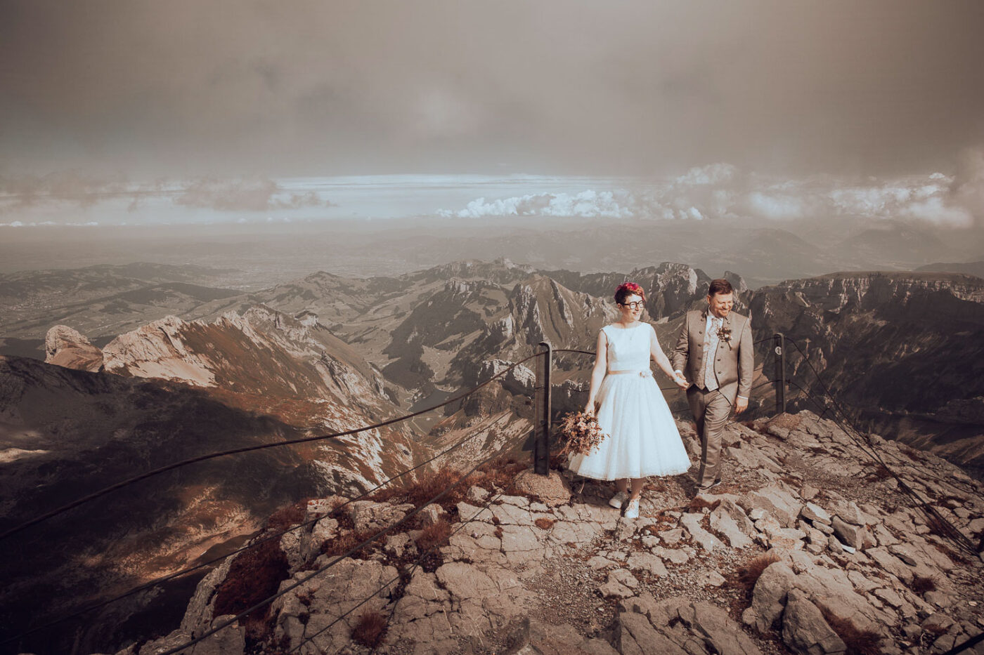 Hochzeitspaar auf dem Säntis mit atemberaubender Aussicht, Braut im Vintage-Kleid und Bräutigam in traditionellem Hochzeitsanzug.