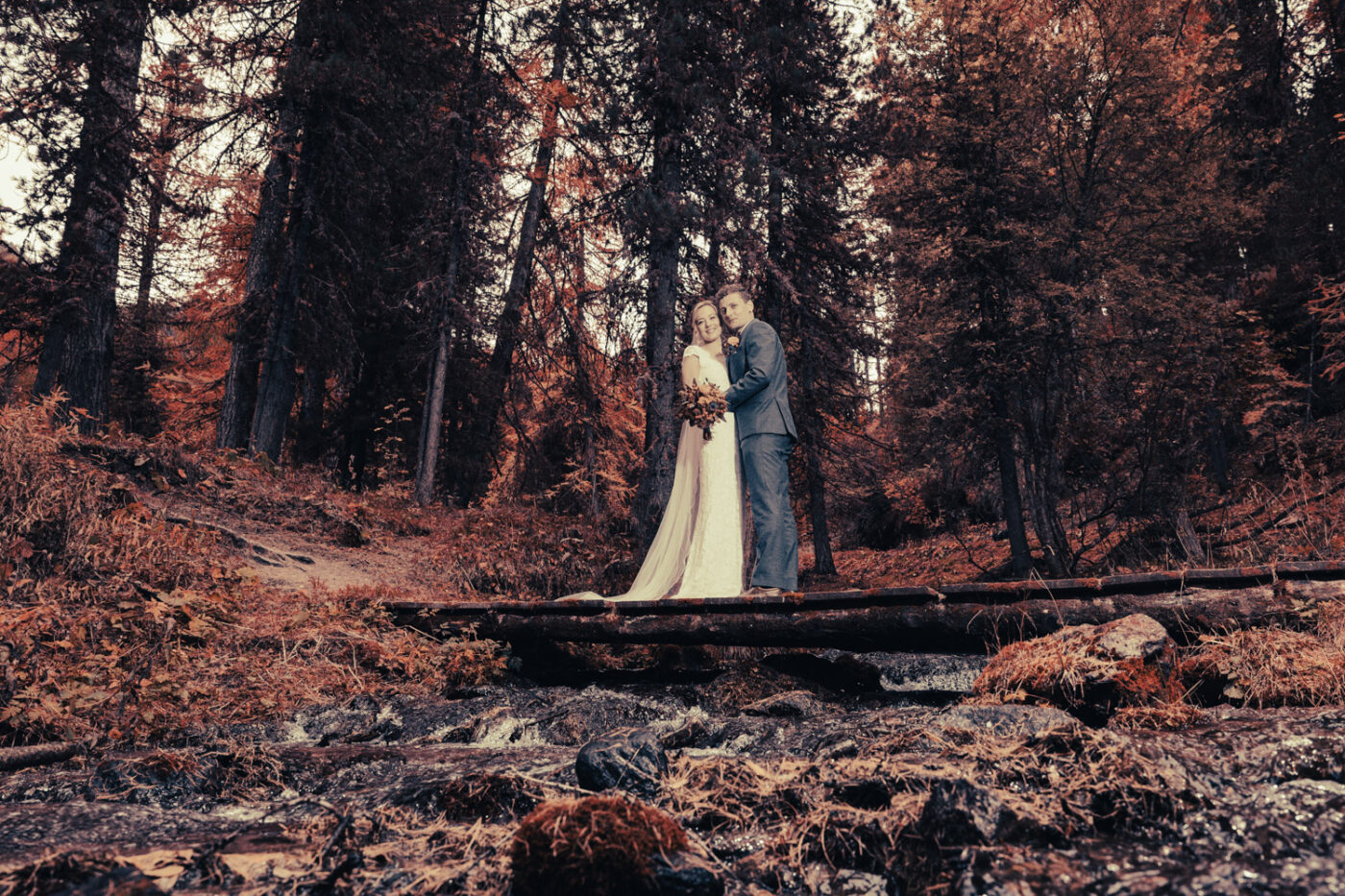 Brautpaar im herbstlichen Wald auf einer Brücke, fotografiert von Hochzeitsfotograf Adrian Flütsch beim Hotel Bellavista im Engadin.