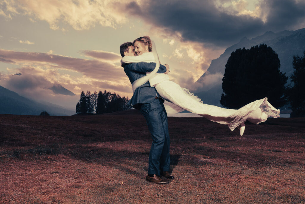 Romantisches Hochzeitsfoto von Deborah und Patrick vor einer dramatischen Abendkulisse im Engadin, aufgenommen von dem bekannten Hochzeitsfotografen Adrian Flütsch.