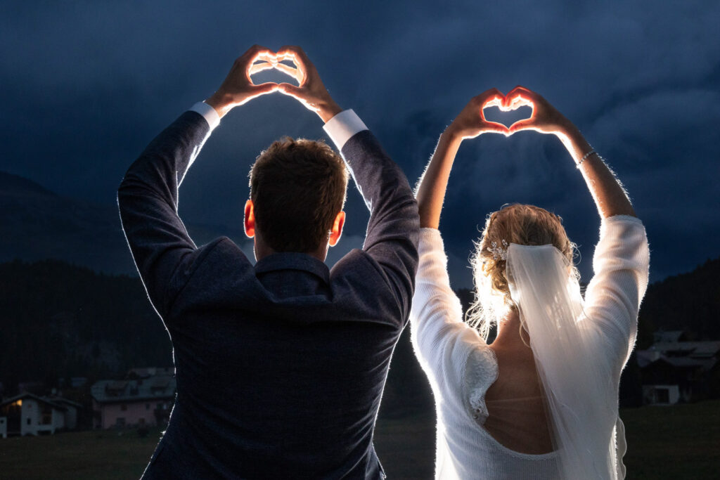 Romantisches Hochzeitsfoto im Engadin: Brautpaar formt gemeinsam Herzsymbol mit ihren Händen, fotografiert von Adrian Flütsch, einem renommierten Hochzeitsfotografen.