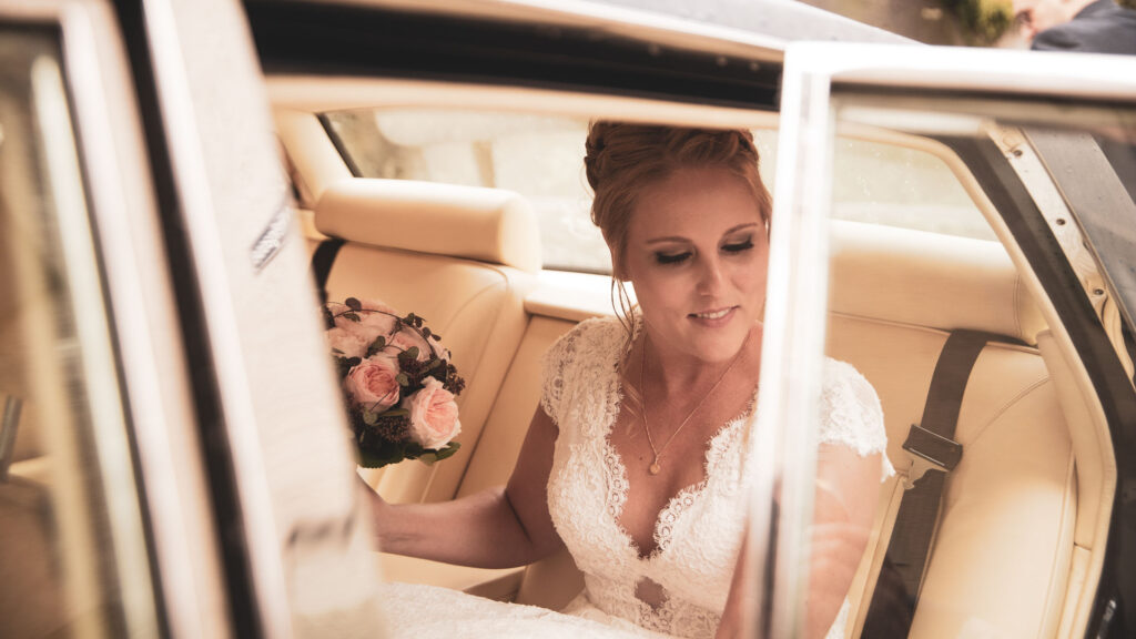 Braut im Hochzeitsauto mit Blumenstrauß, fotografiert von Adrian Flütsch.