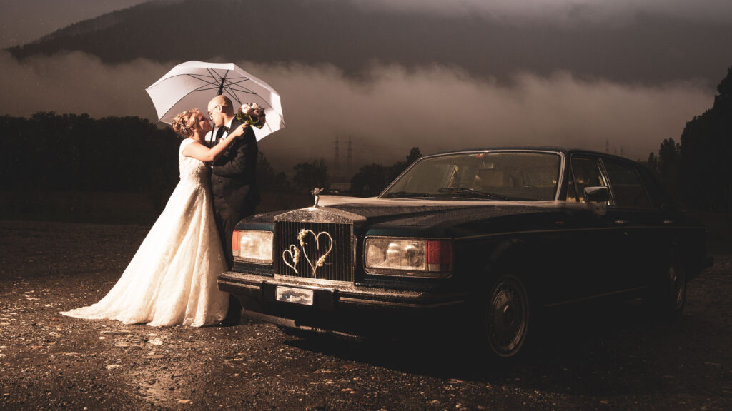 Hochzeitspaar vor einem Rolls-Royce im Regen – Hochzeitsfotograf Adrian Flütsch, Graubünden